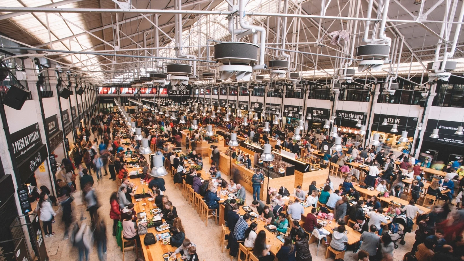A bustling indoor food hall with communal tables and warm lighting as people eat and chat