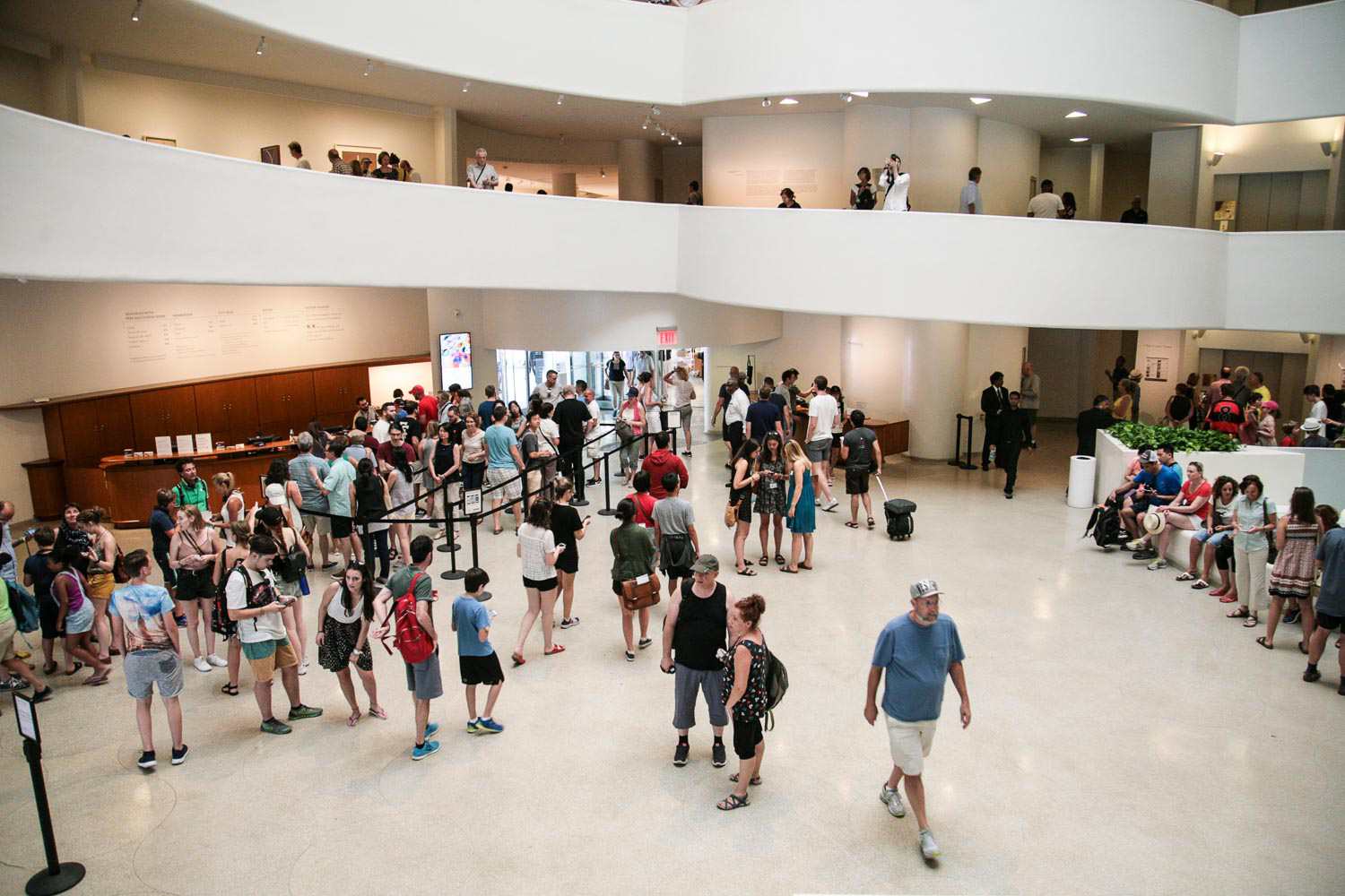 A busy museum lobby at midday with visitors lining up for tickets and families gathering near the entrance
