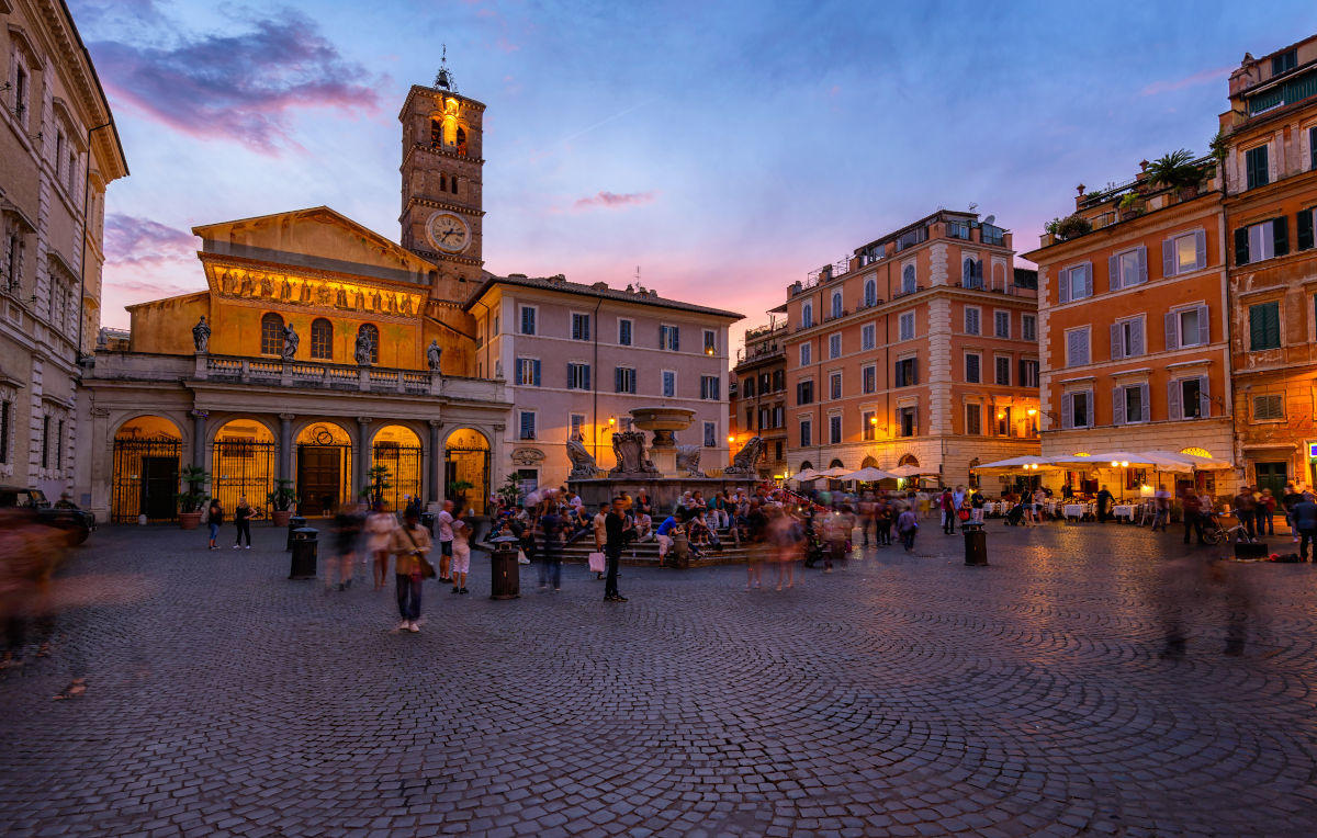 A couple strolling down a lively European city street at dusk with warm restaurant lights, gelato in hand, and historic buildings in the background