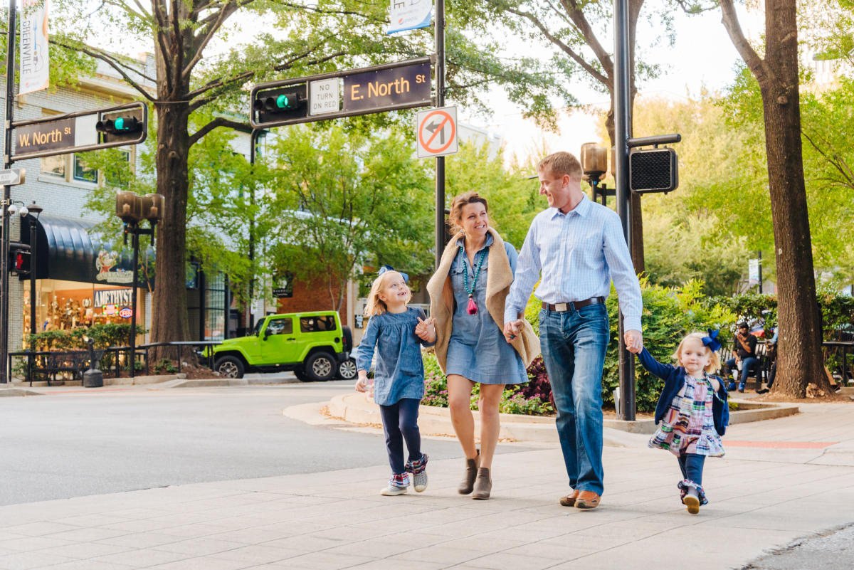 A family pushing a stroller while walking through a busy downtown area with attractions and shops nearby