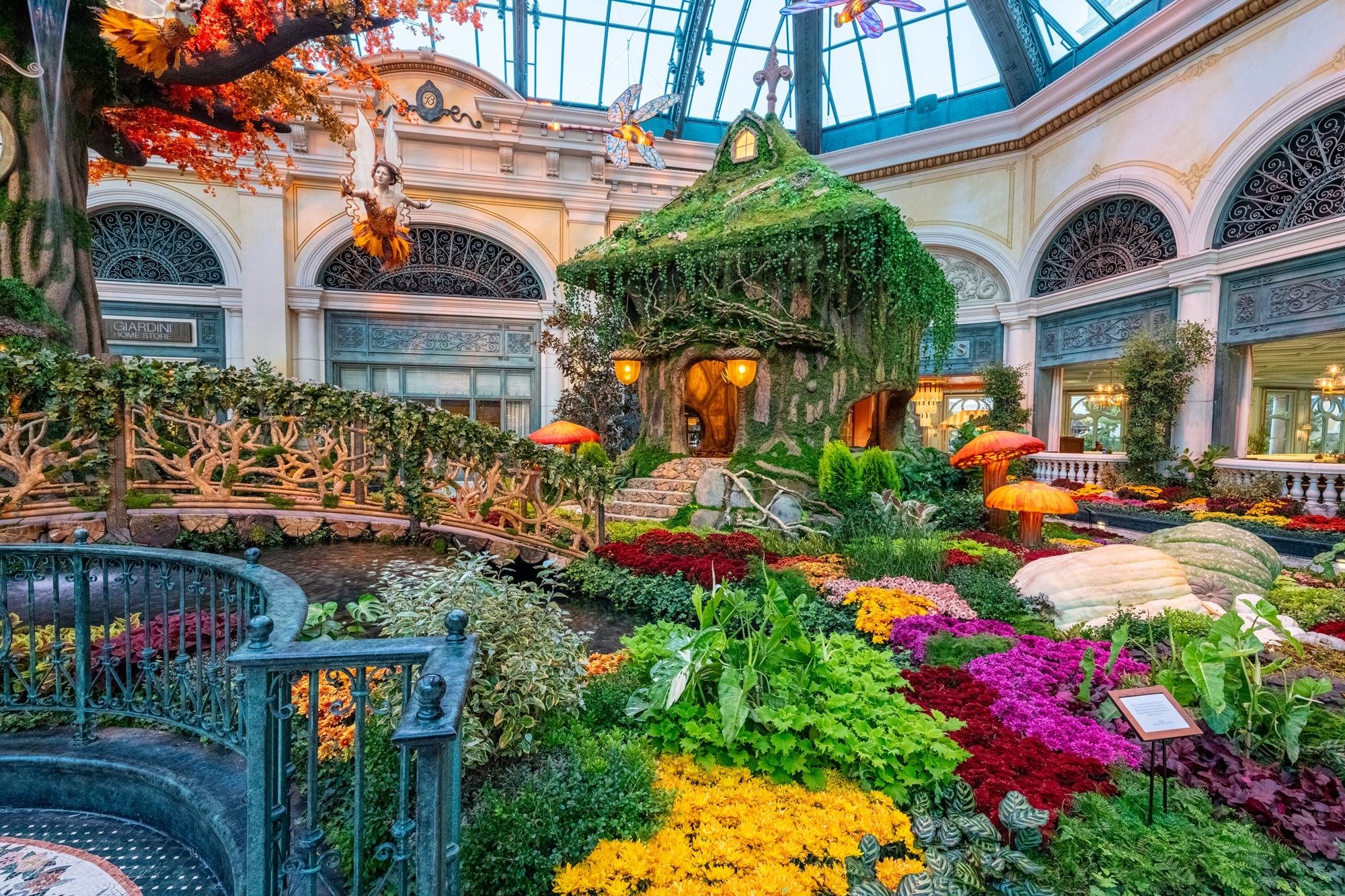 A lush indoor conservatory with seasonal floral arrangements and visitors strolling along a pathway