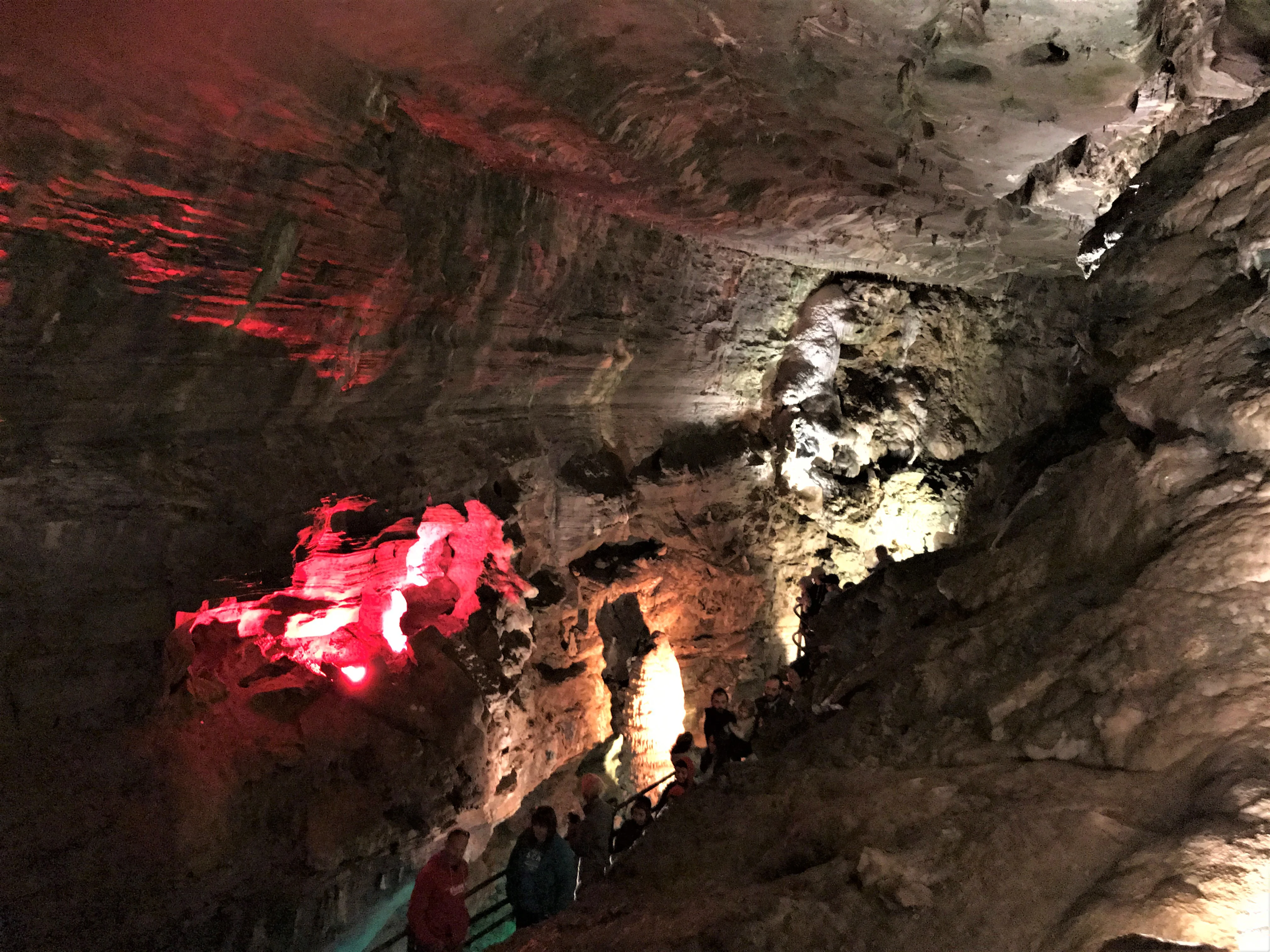 A narrow cavern stairway with handrails and visitors walking in single file under low rock ceilings