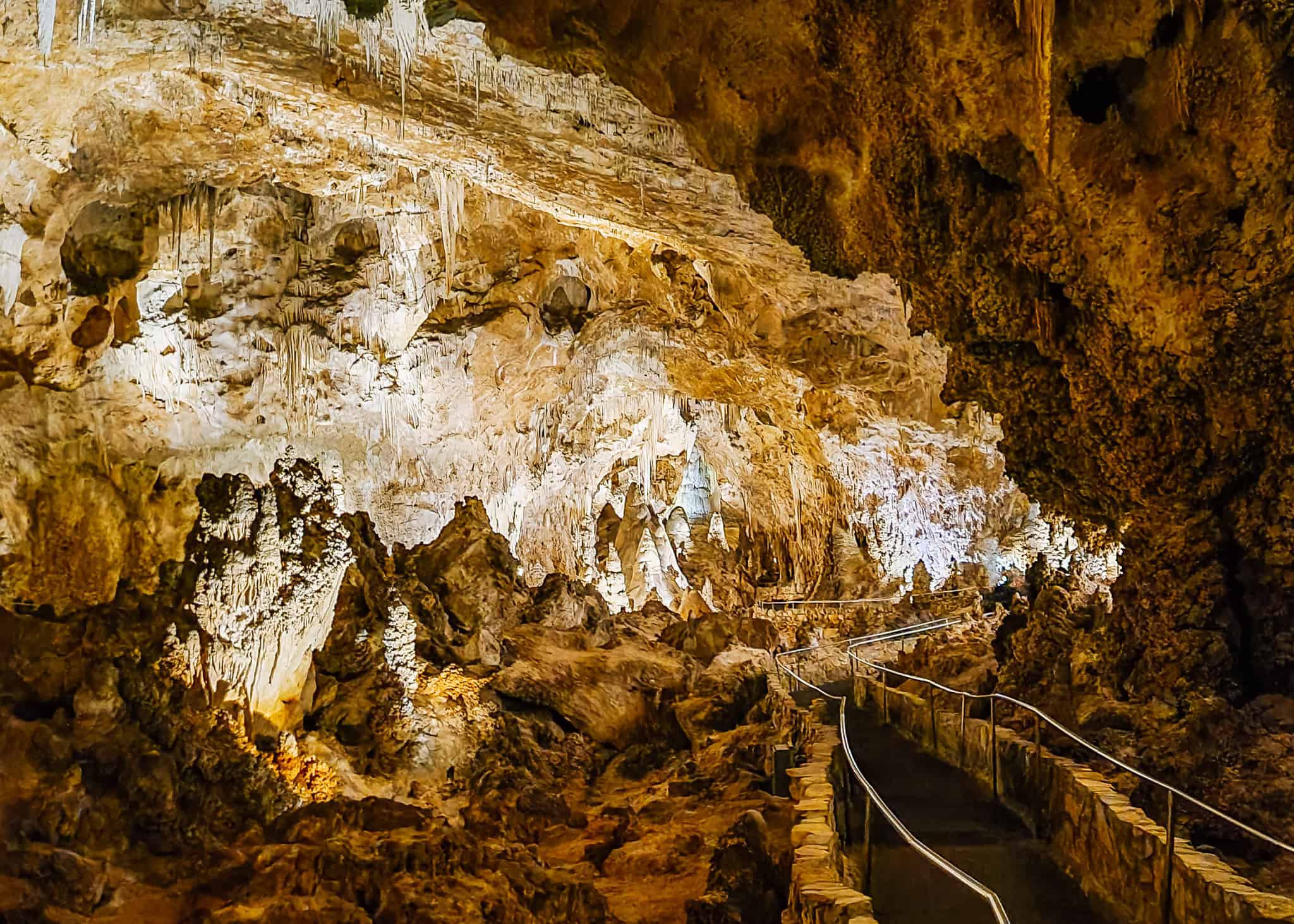 A parent holding a young child’s hand on a well-lit cavern walkway with railings and large rock formations