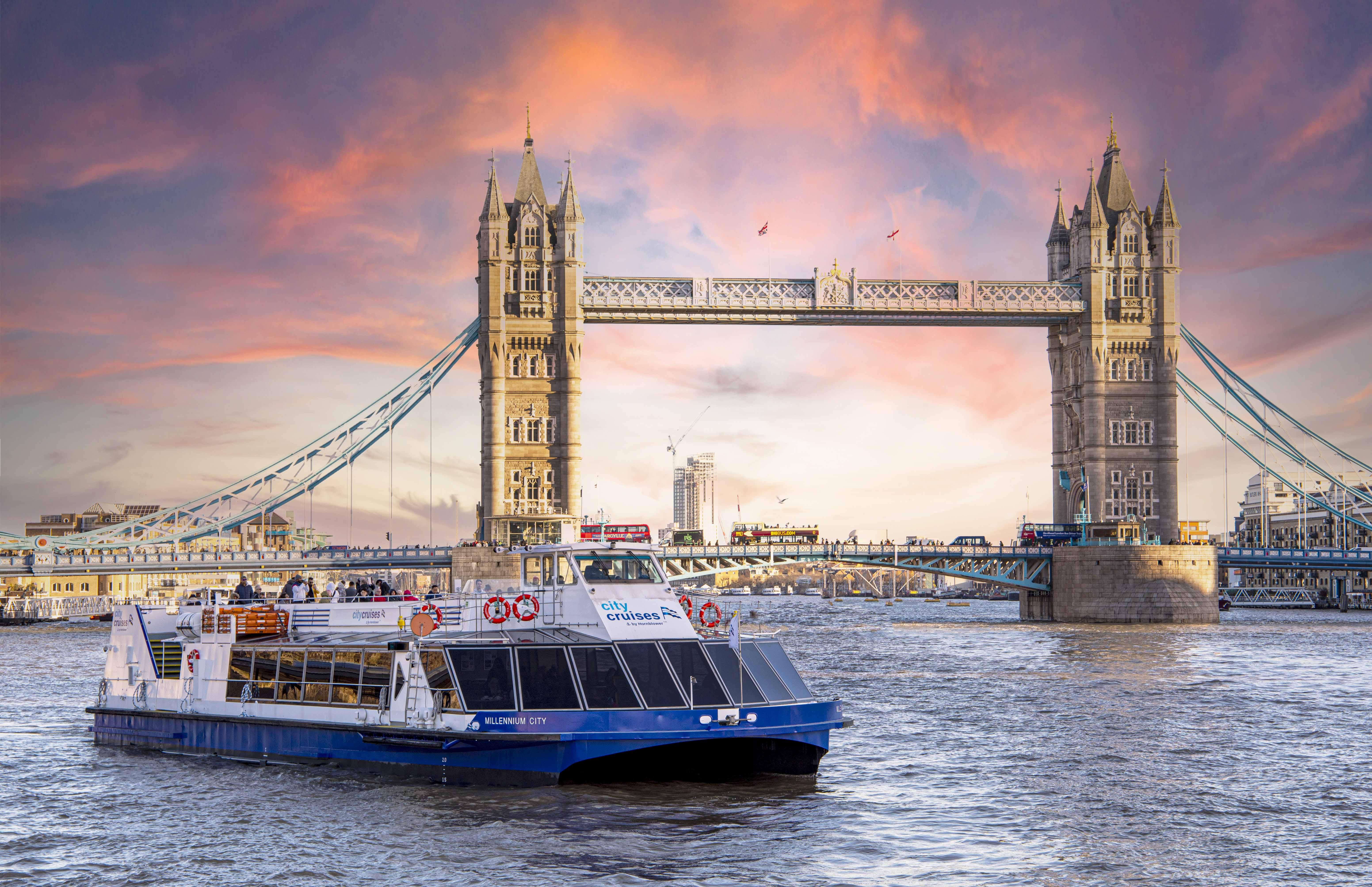 A sightseeing boat on the River Thames in London passing under a bridge with passengers seated on the upper deck