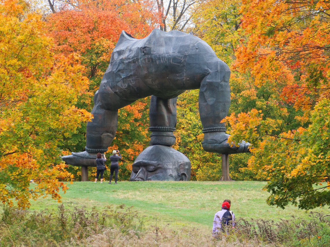 A smooth path winding through a green lawn with a large outdoor sculpture in the distance and tree-covered hills behind