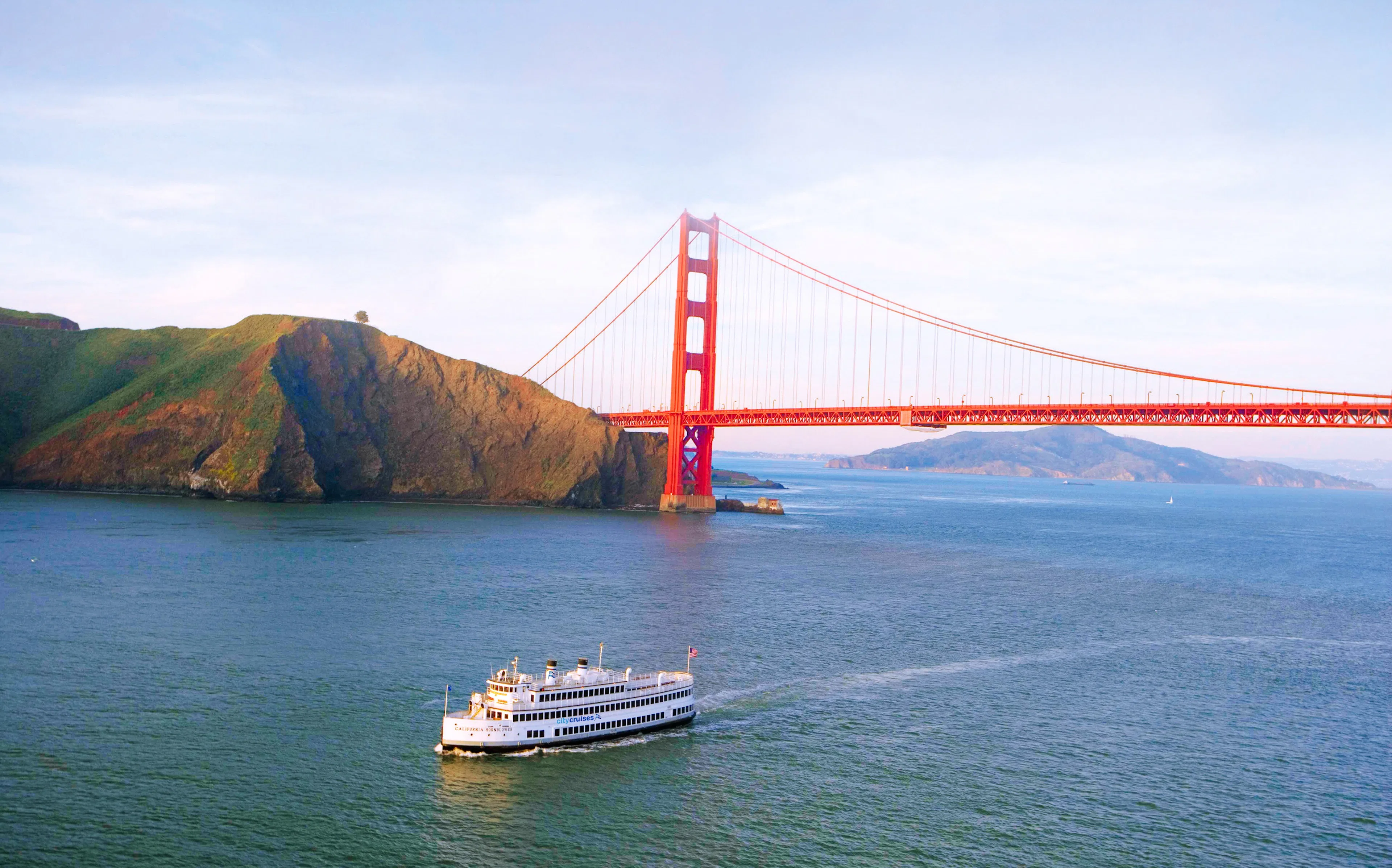 A tour boat cruising in San Francisco Bay with the city skyline in the distance and passengers taking photos from the open deck
