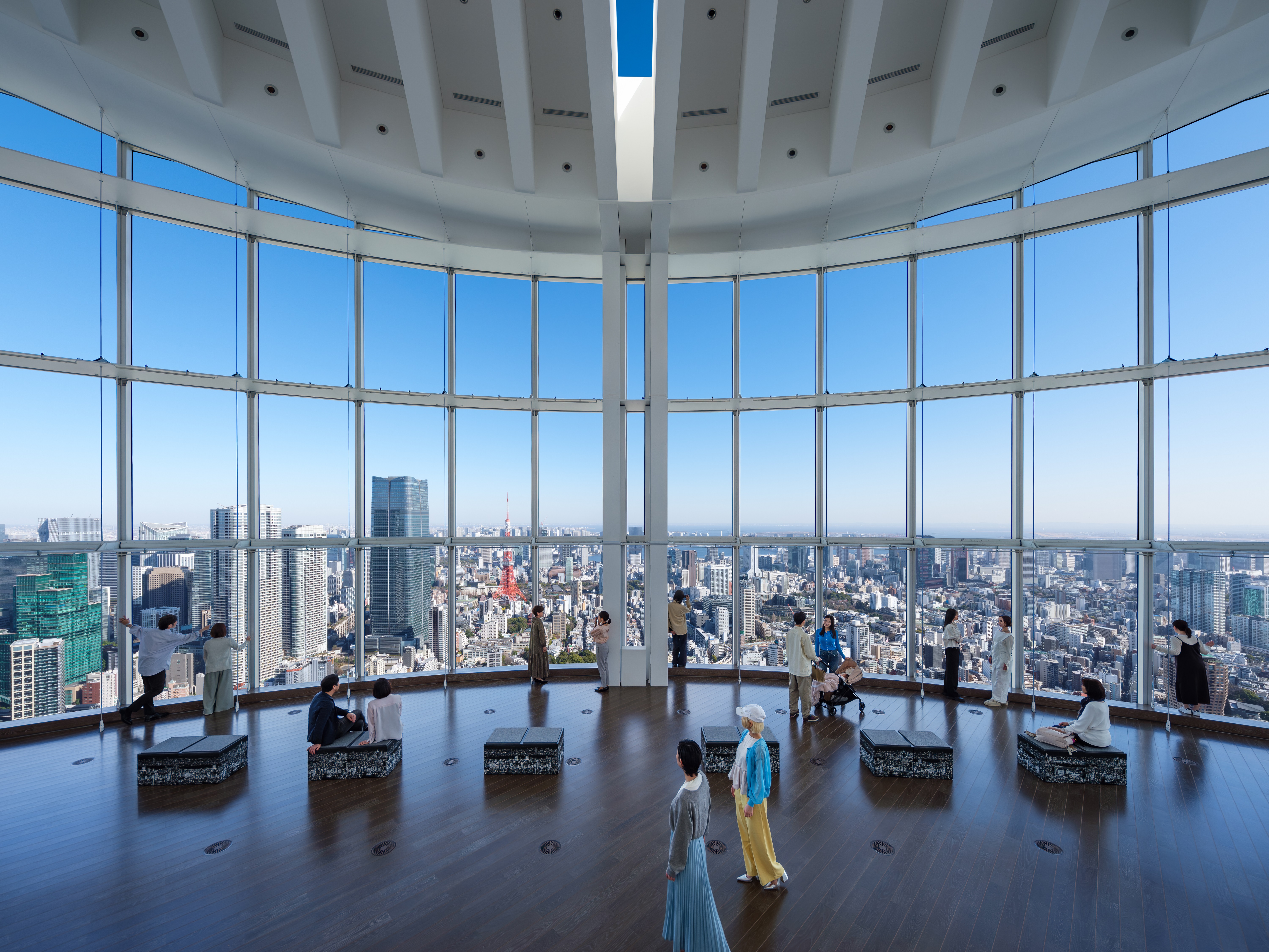 Visitors looking out through tall glass windows at a rainy city skyline from an indoor observation deck