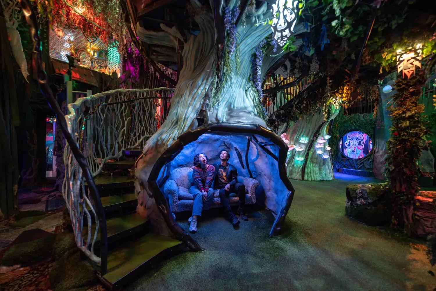 Visitors walking through a vivid, otherworldly immersive art room with glowing colors and sculptural details